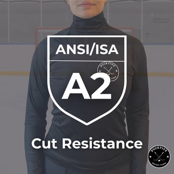 Person wearing a black long-sleeve shirt with ANSI/ISA A2 cut resistance label on a blurred hockey rink background.