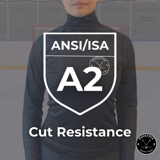 Person wearing a black long-sleeve shirt with ANSI/ISA A2 cut resistance label on a blurred hockey rink background.