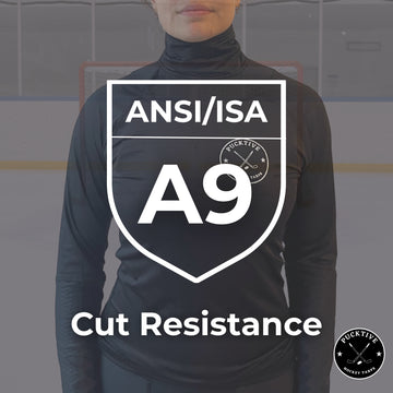 Person wearing a black long-sleeve shirt with ANSI/ISA A9 cut resistance certification on a blurred hockey rink background.