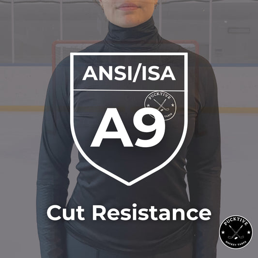 Person wearing a black long-sleeve shirt with ANSI/ISA A9 cut resistance certification on a blurred hockey rink background.