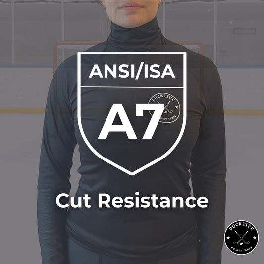 Person wearing a black turtleneck with ANSI/ISA A7 cut resistance label on a blurred hockey rink background.